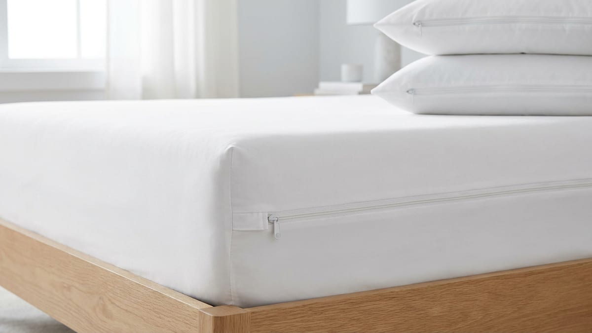 Coin d'un matelas enveloppé dans une housse intégrale blanche, fermeture éclair le long du bord, oreillers protégés posés à côté
